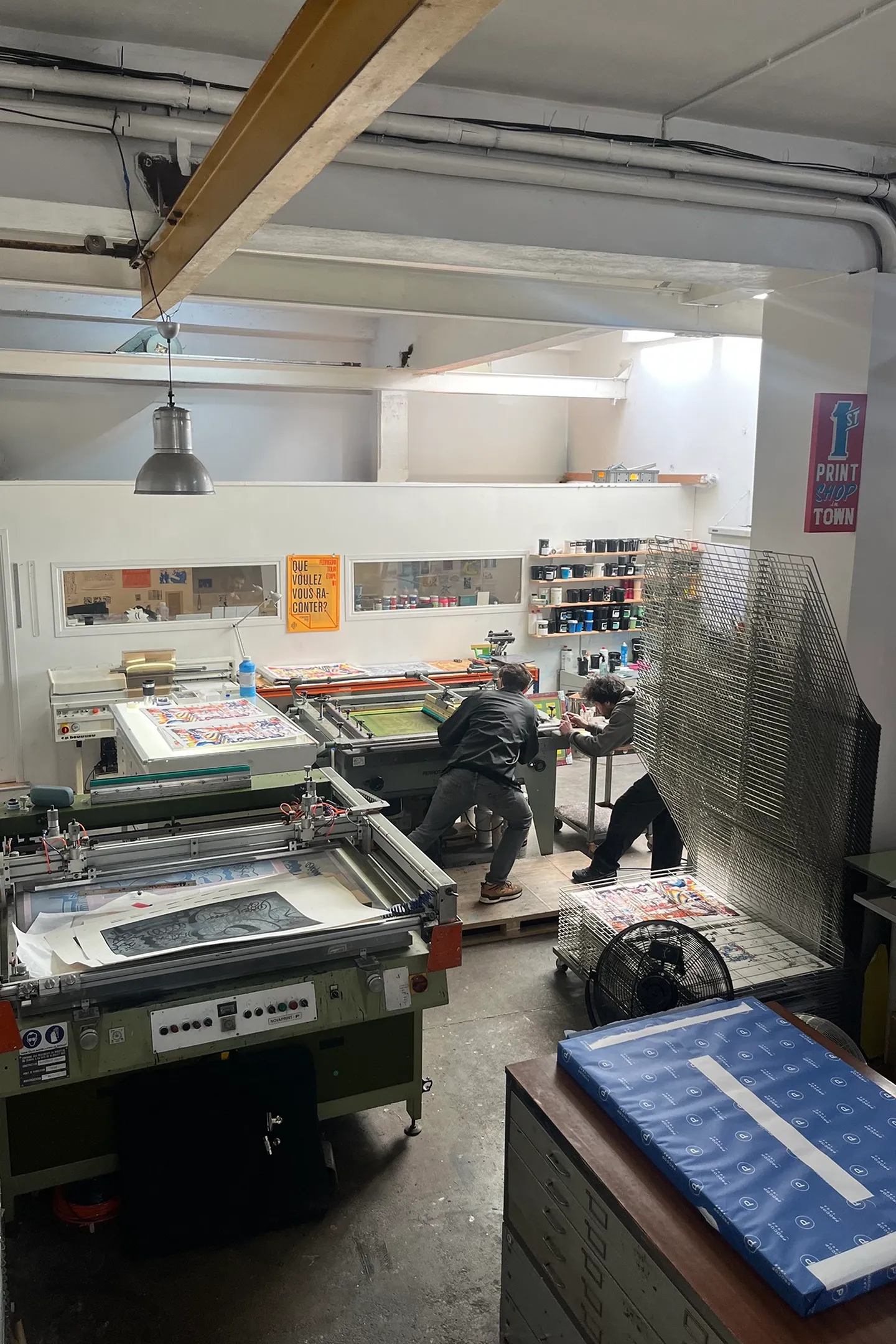 Vue intérieure de l’atelier de sérigraphie avec les presses et les claies de séchage.